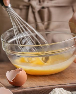 Female,Chef,Whisking,Eggs,In,Glass,Bowl,On,Kitchen,Table